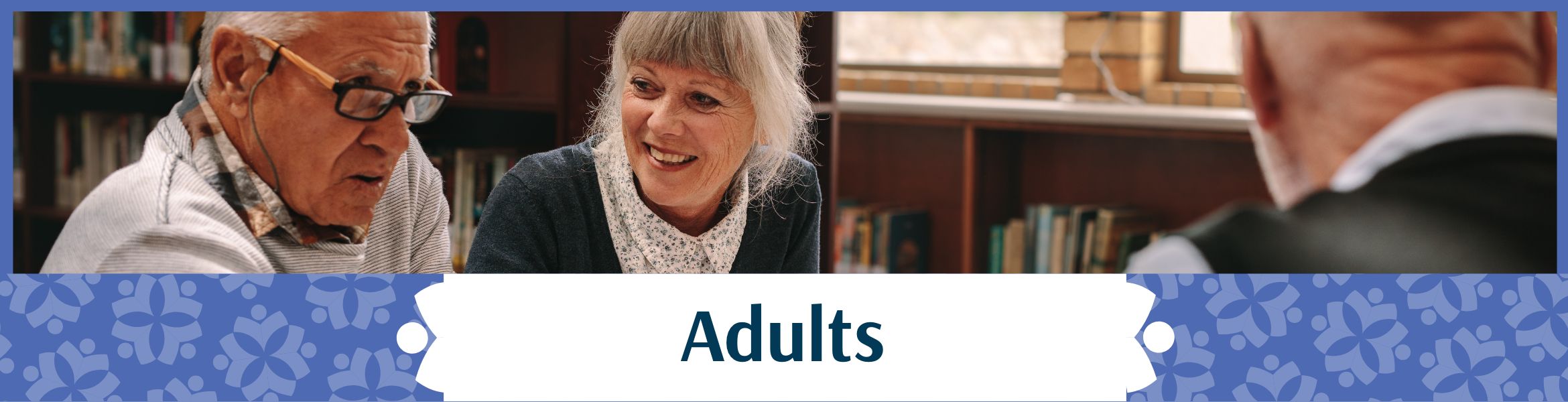 Adults header image showing a group of three seniors, two men and a woman, sitting at a table in the library mid-conversation