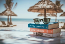 Stack of books with straw patio umbrellas with sand and beach in the background