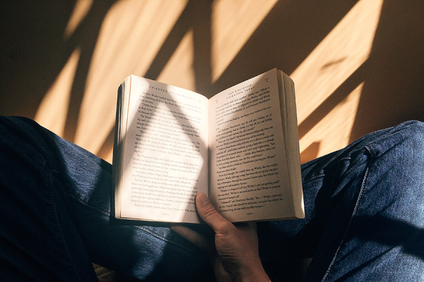 Person sitting crossed-legged on floor with open book in hand