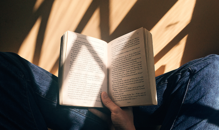 Person sitting crossed-legged on floor with open book in hand